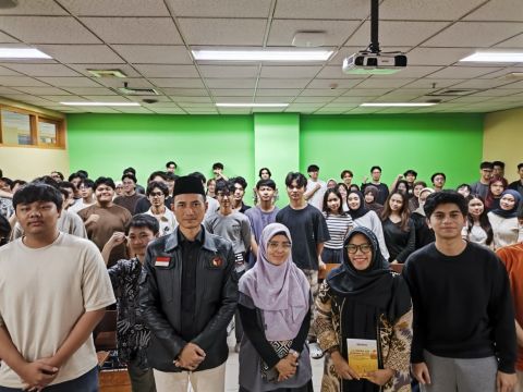 Ketua Bawaslu Provinsi DKI Jakarta berdiri di barisan depan bersama beberapa staf, berfoto dengan mahasiswa Binus yang memenuhi ruangan kelas, dengan latar dinding hijau dan perangkat proyektor di atas
